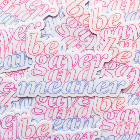 Photo of a white sticker with the words 'be gayer and meaner' in pride flag colours of red, orange, pink and blue.