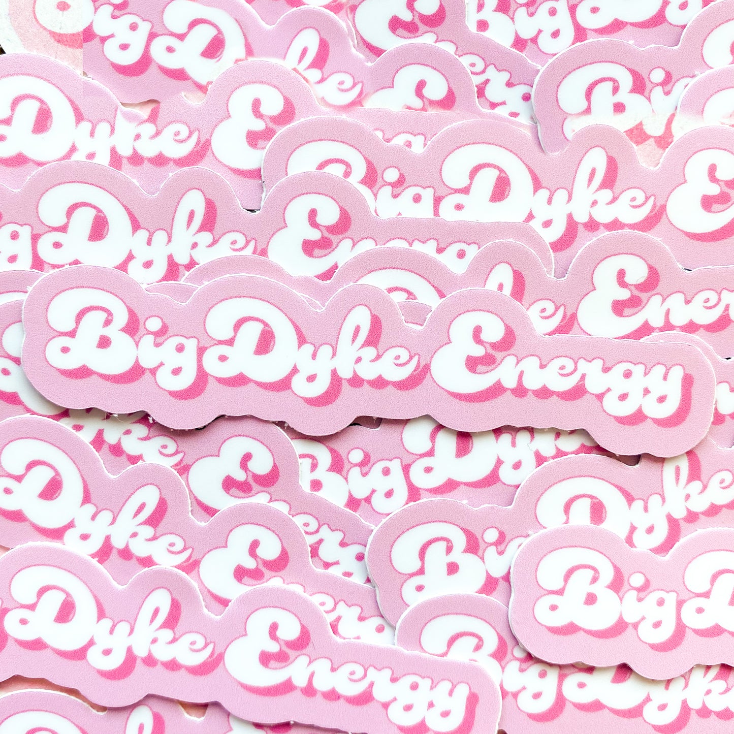 Photo of pink and white sticker with the words 'big dyke energy', a funny lesbian pun.